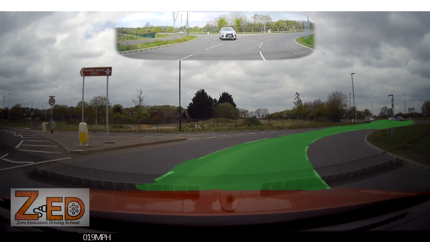Car dashboard camera view of a roundabout with cloudy sky and road signs.