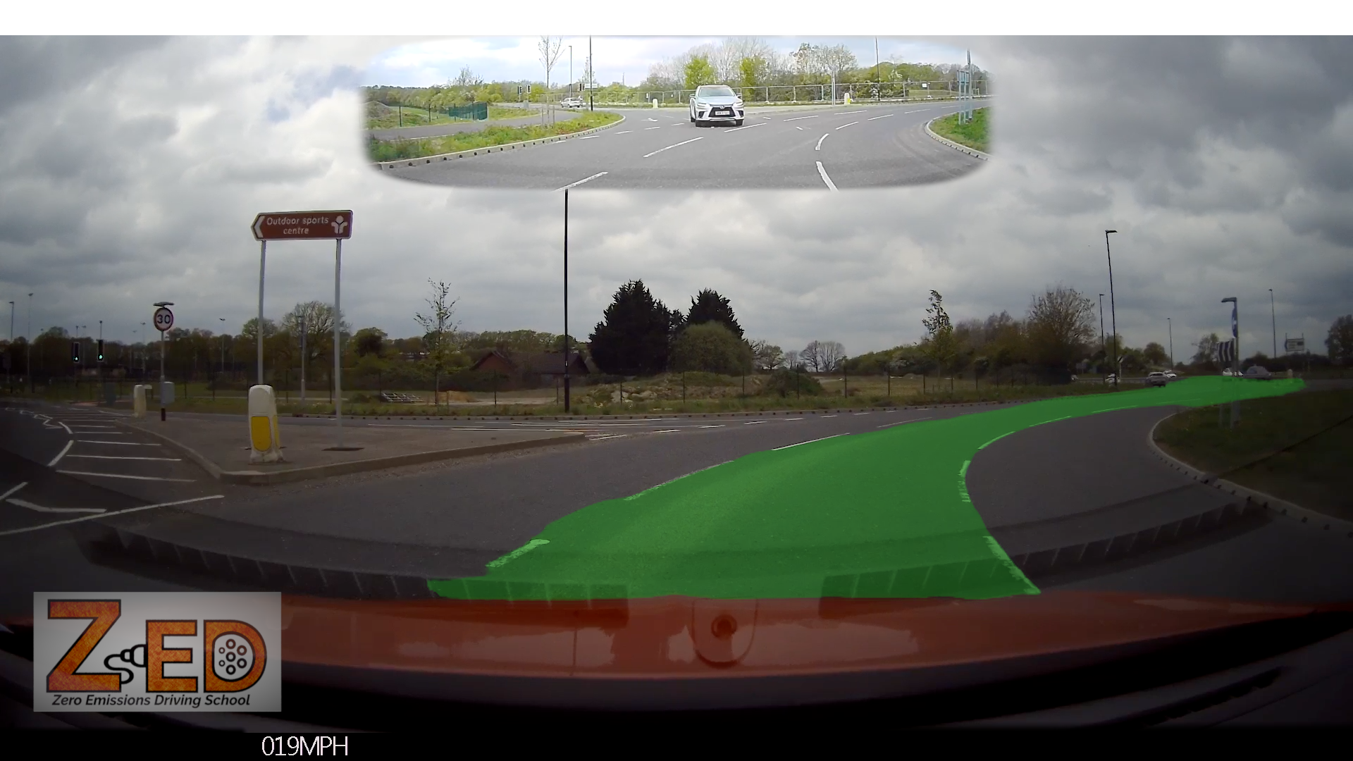 Car dashboard camera view of a roundabout with cloudy sky and road signs.