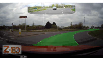 Car dashboard camera view of a roundabout with cloudy sky and road signs.