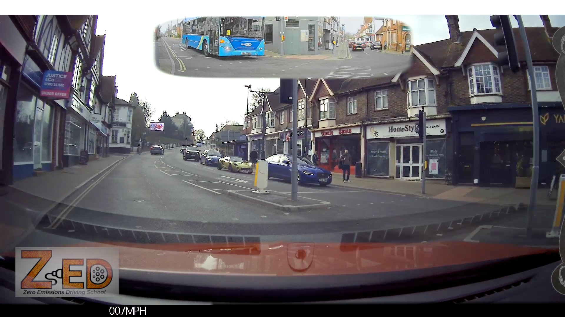 Dashcam view of a street with buildings and cars, including a ZED logo.