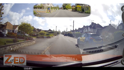 Car dashboard view with a ZED device displaying speed, showing a residential street.