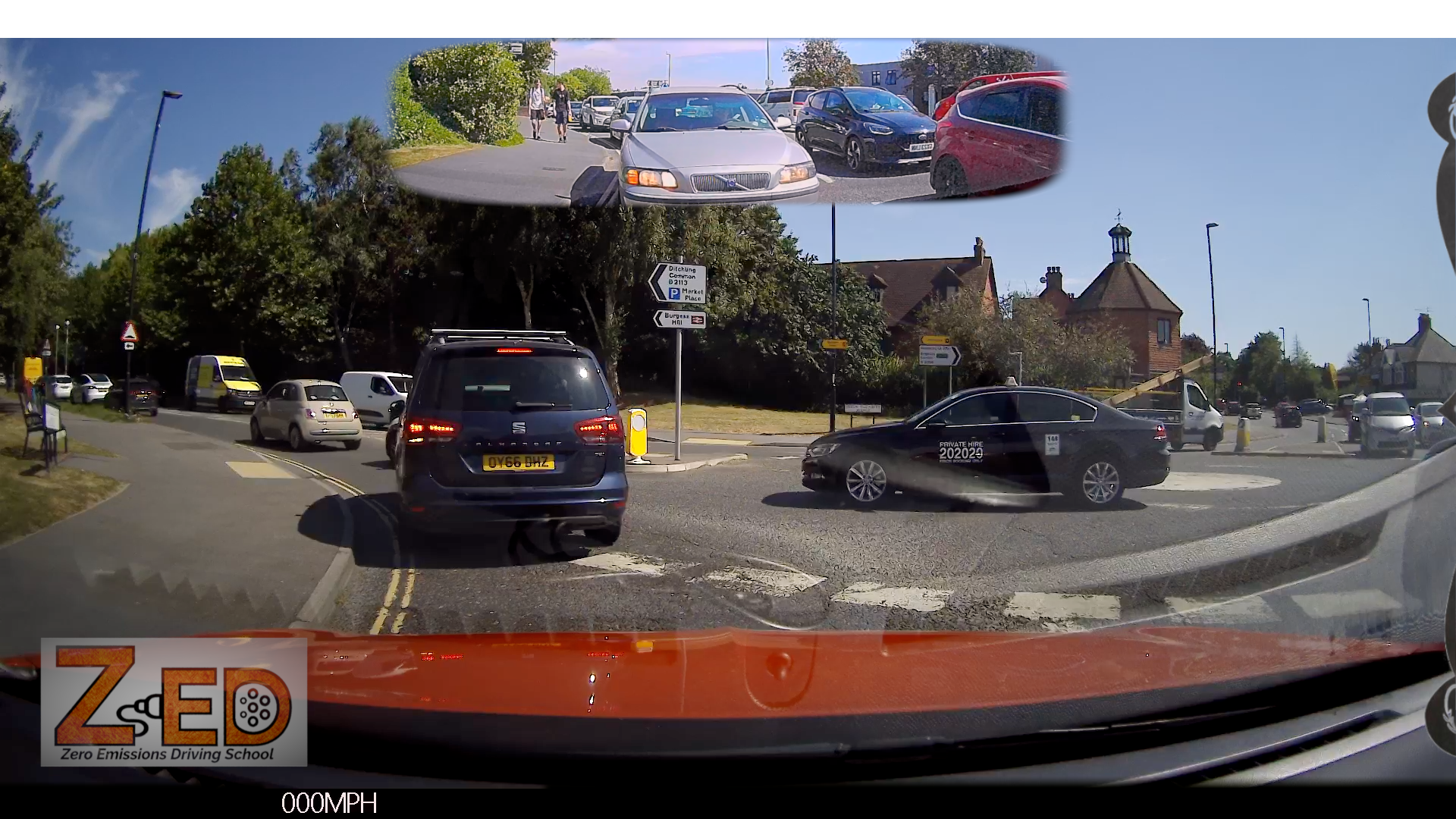 A rear-view dashcam scene from inside a vehicle at an intersection, with a blue minivan directly behind, a black sedan turning right, trees, buildings, and a small inset mirror-like reflection at the top. A large 'ZED' watermark appears in the lower left.
