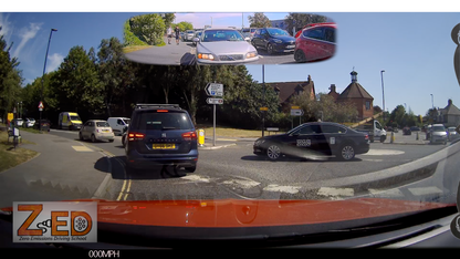 A rear-view dashcam scene from inside a vehicle at an intersection, with a blue minivan directly behind, a black sedan turning right, trees, buildings, and a small inset mirror-like reflection at the top. A large 'ZED' watermark appears in the lower left.